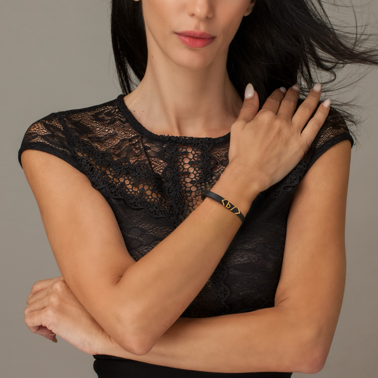 Woman wearing a black leather bracelet with a html bold tag code charm for boldness and strength